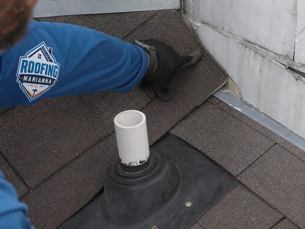 Inspector indicating wear around roof flashing, shingle edges, and a plumbing vent boot